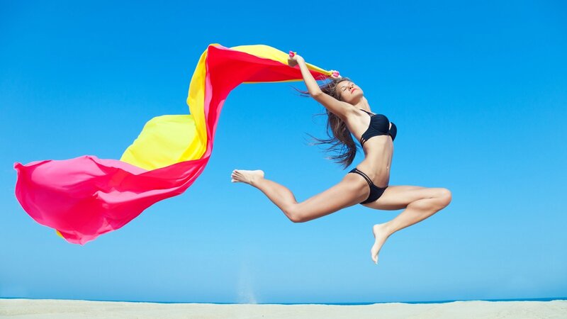 Woman jumping with scarf at beach