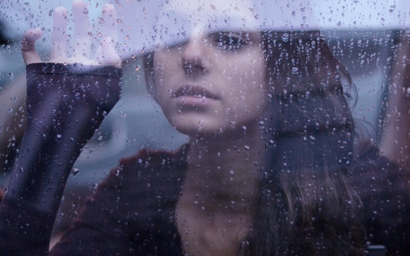 woman looking through rain-covered window