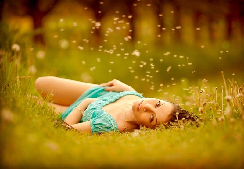 Woman lying in grass with dandelion seeds