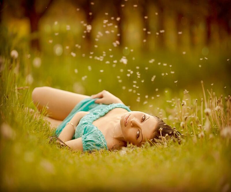 Woman lying in grass with dandelion seeds