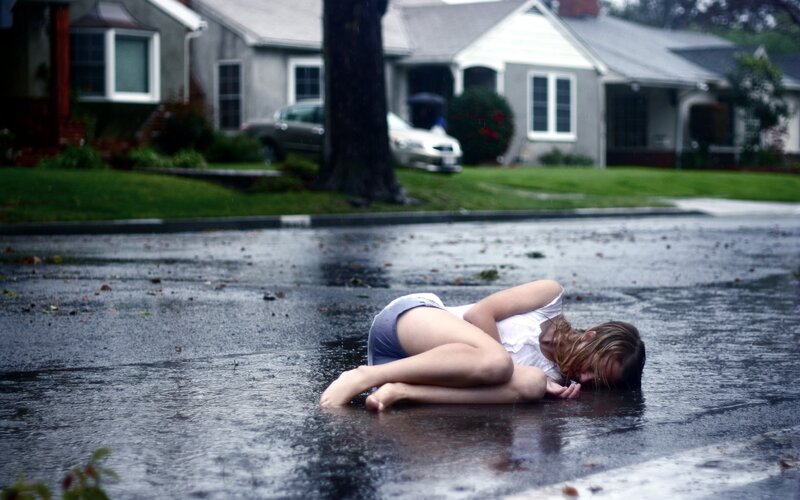 Woman lying in rain on street