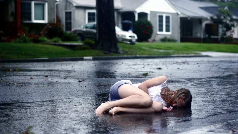 Woman lying in rain on street