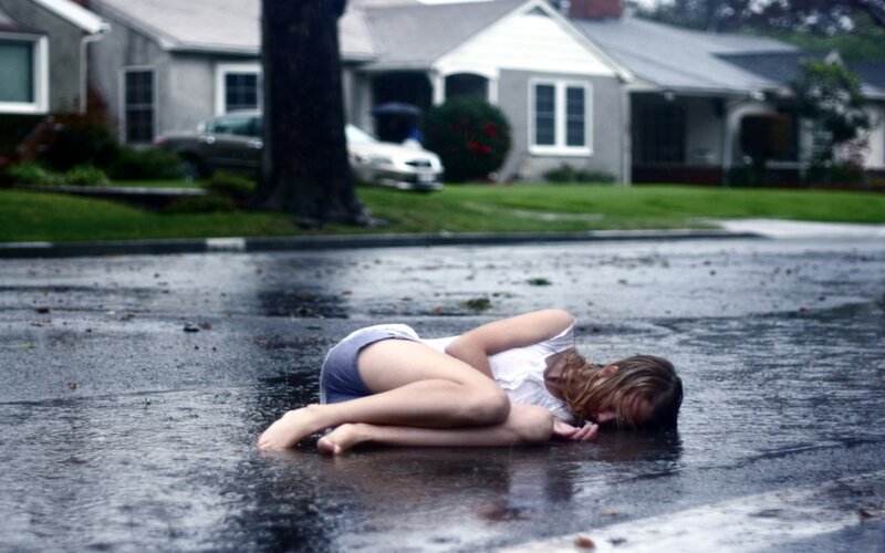 Woman lying in rain on street
