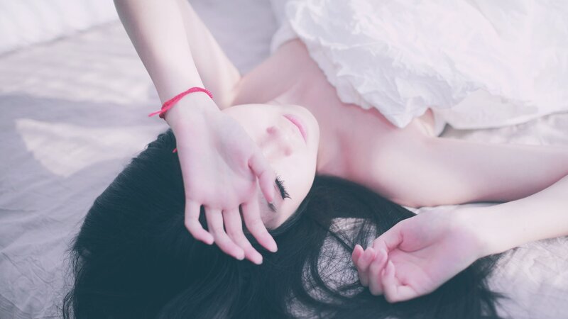woman lying on bed with hand over face