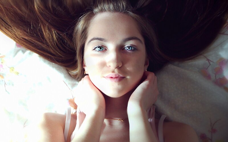 woman lying on bed with hands under chin