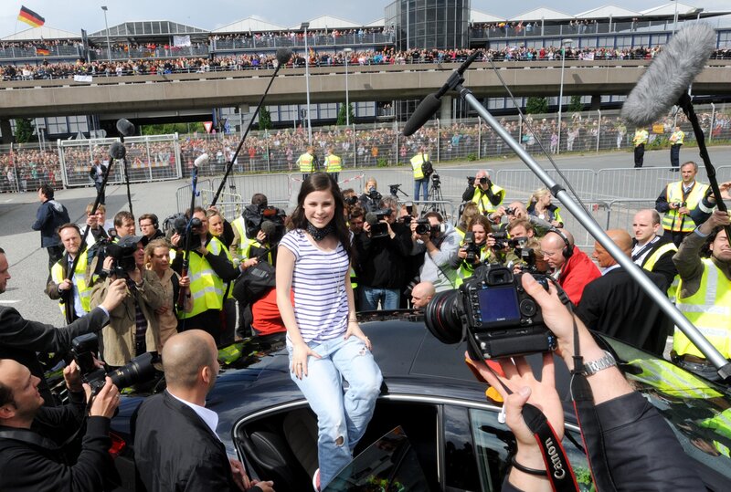 Woman on car surrounded by press