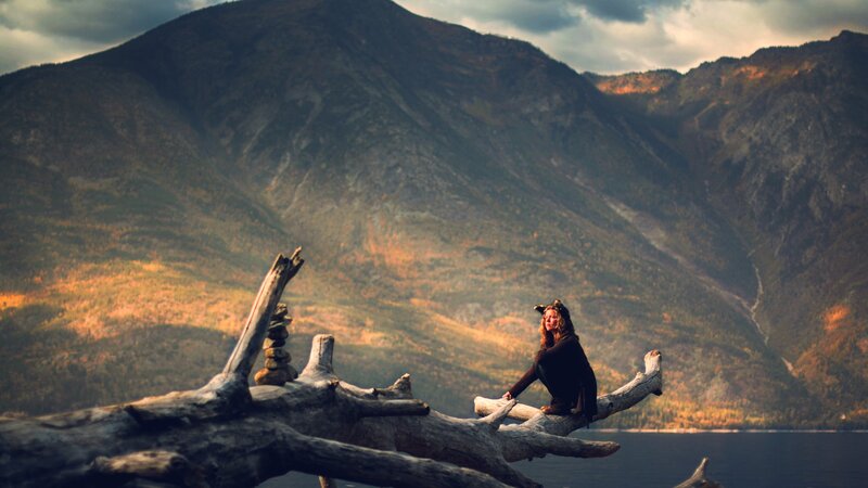 Woman on driftwood by mountain lake