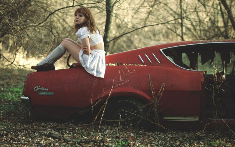 Woman on red car in woods