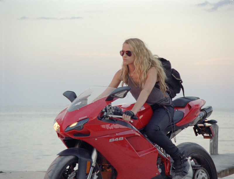 Woman on red motorcycle by water