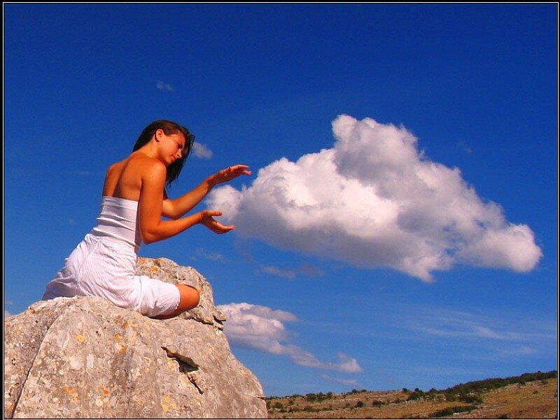 Woman on rock reaching for cloud