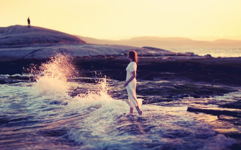 Woman on rocky shore at sunset