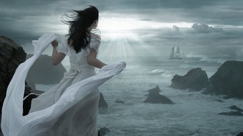 woman on rocky shore watching ship