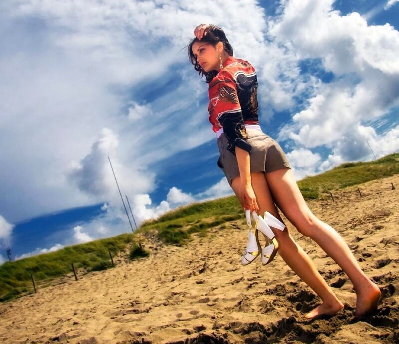woman on sandy dune holding shoes