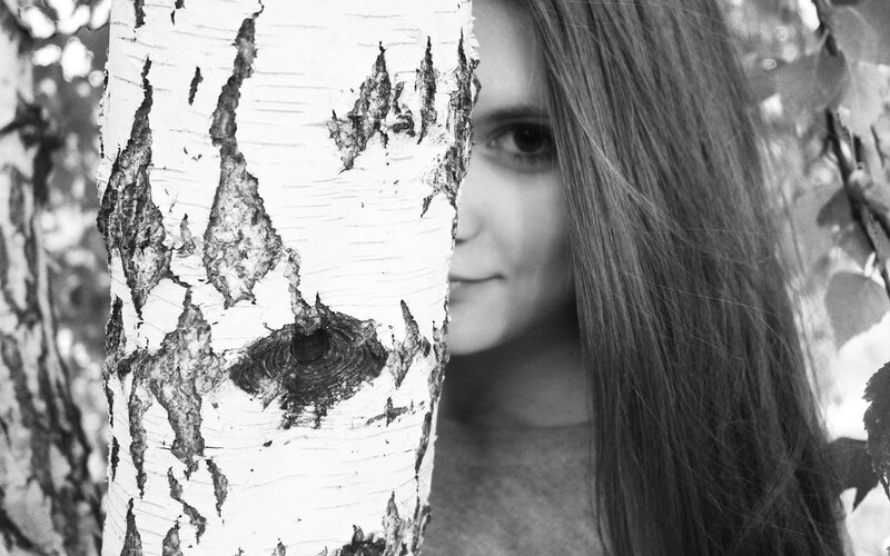 woman peeking from behind a birch tree
