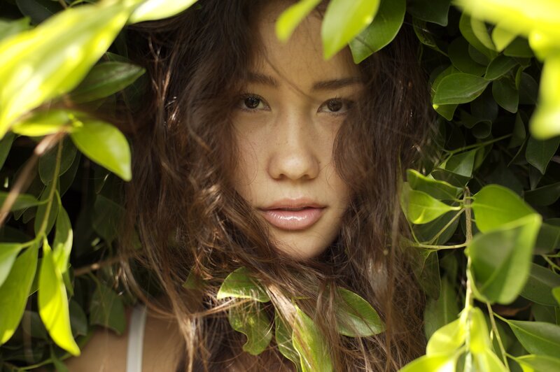 woman peeking through green leaves