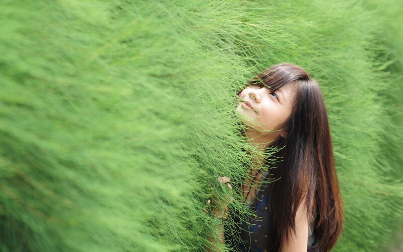 woman peeking through green plants
