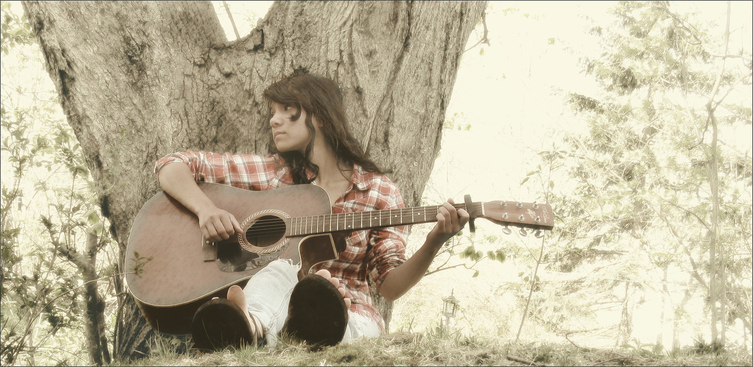 woman playing guitar under tree