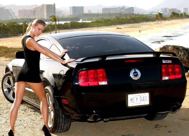 Woman posing with black Ford Mustang