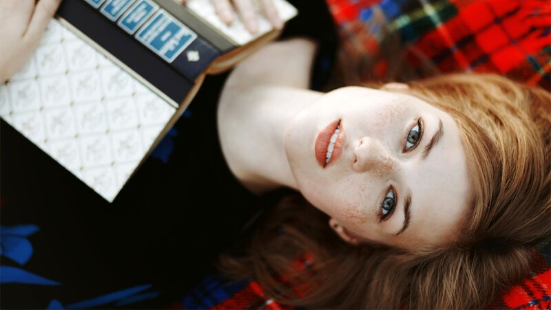 woman reading book on plaid blanket