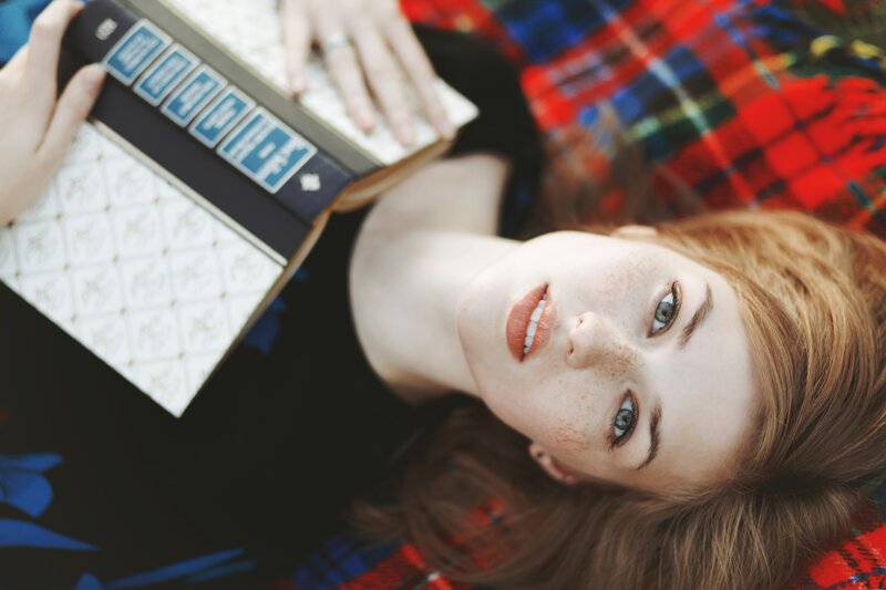 woman reading book on plaid blanket