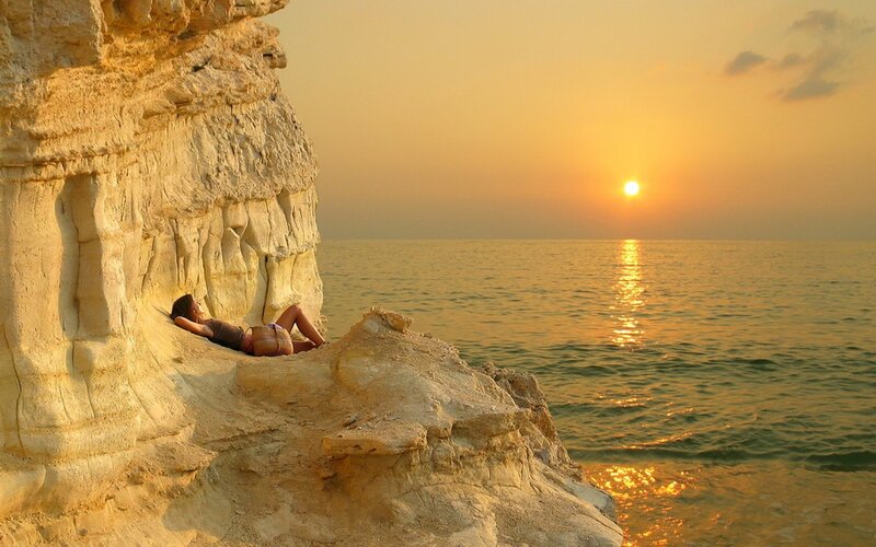Woman relaxing on cliff at sunset