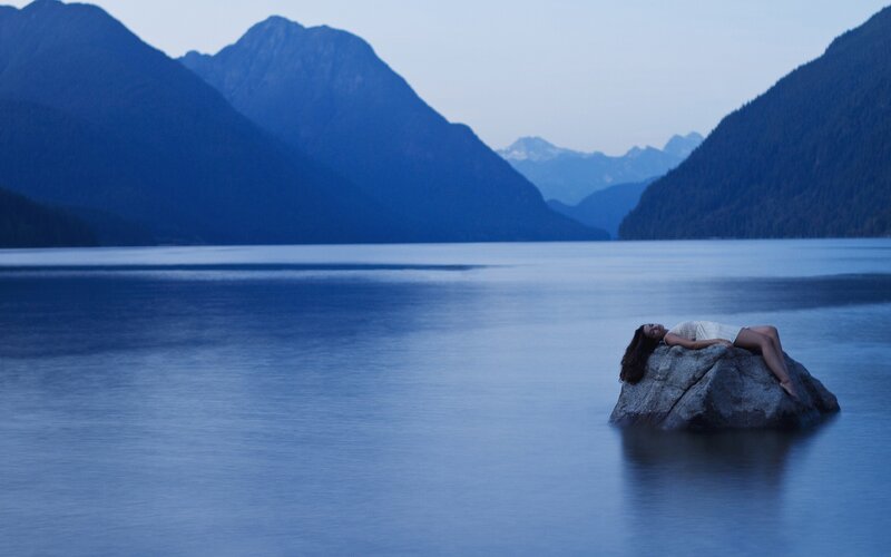 Woman resting on a rock by a lake