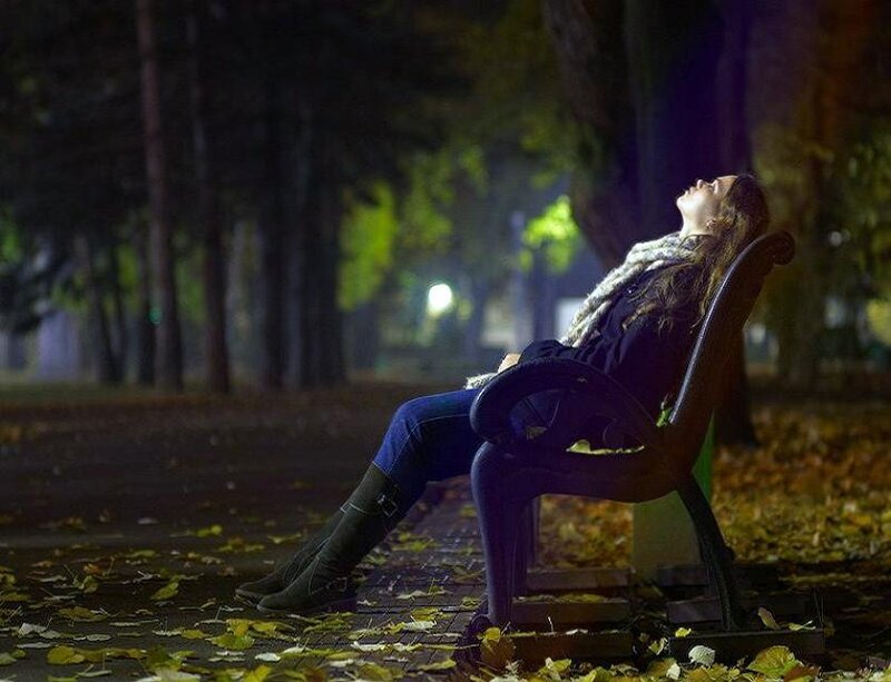 Woman resting on park bench at night