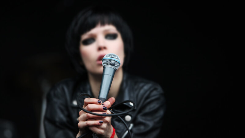 Woman Singing into Microphone — Black, Dramatic, Photograph, Leather Jacket