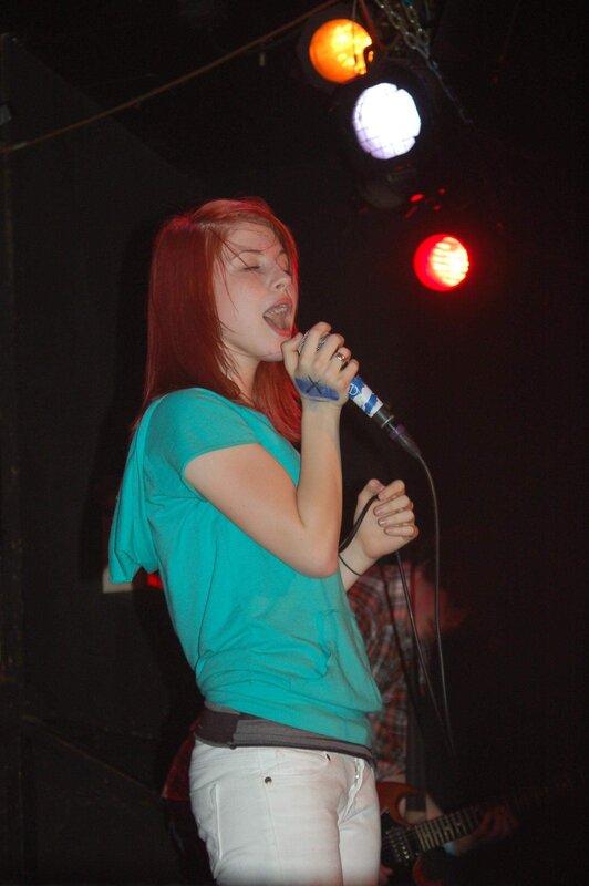 Woman Singing on Stage — Red, Energetic, Night, Photograph, Microphone, Stage Lights, Guitar