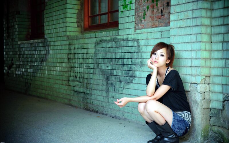 woman sitting against a green brick wall