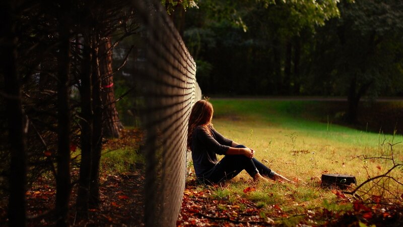woman sitting by fence in park
