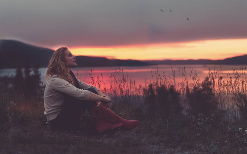 Woman sitting by lake at sunset