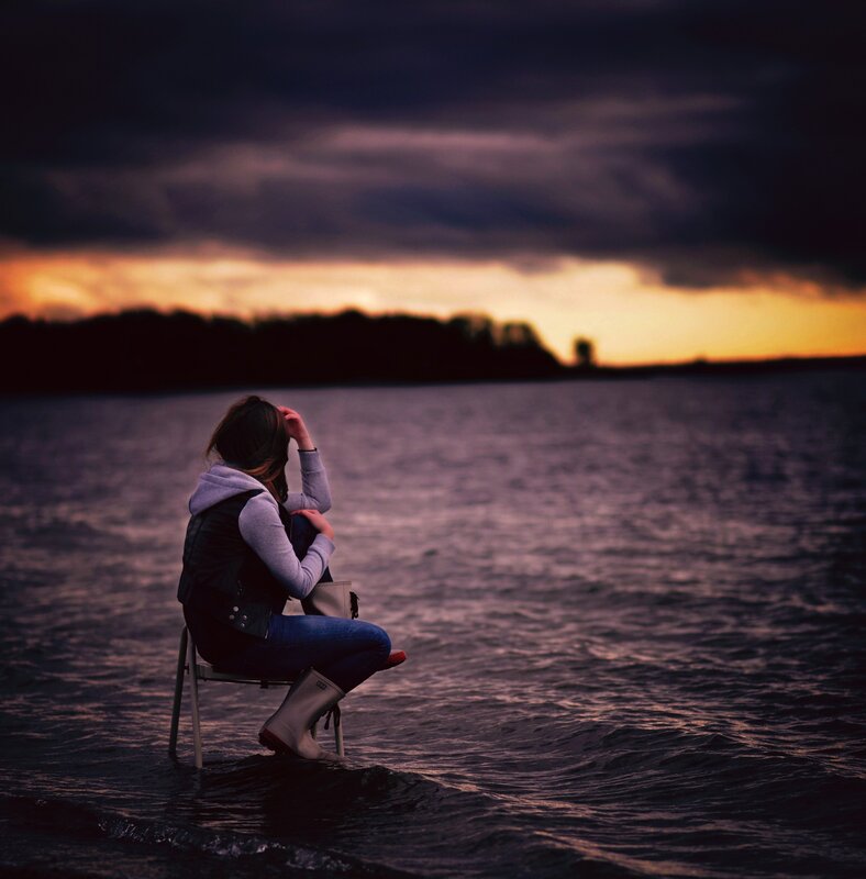 Woman sitting by the water at sunset