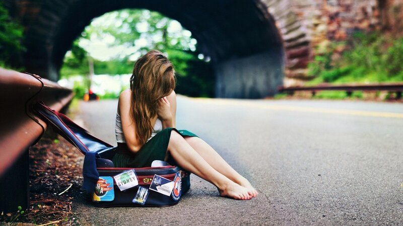 Woman sitting in suitcase by road