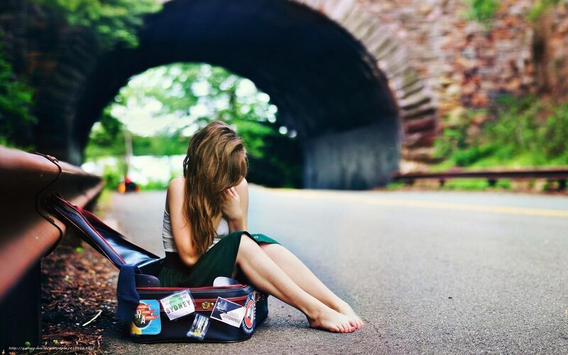 woman sitting in suitcase on road