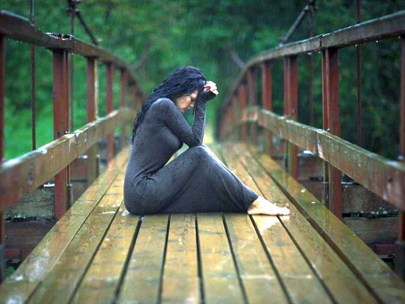 woman sitting on a bridge in rain
