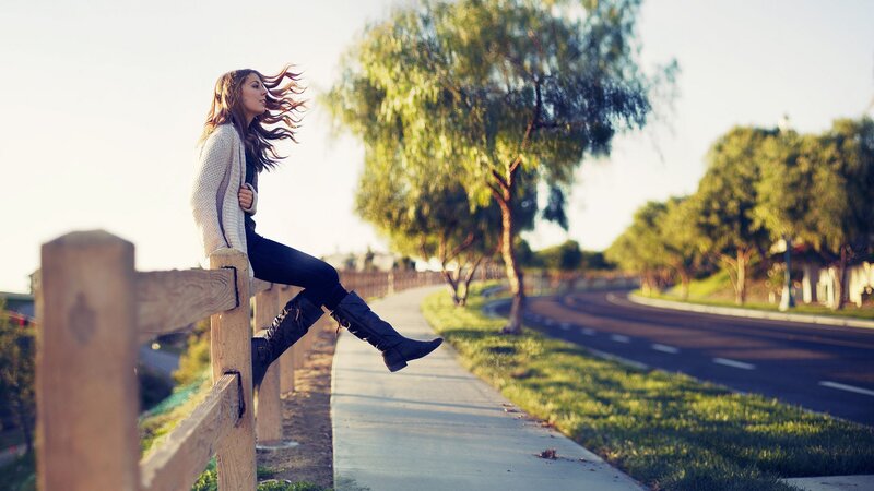 Woman sitting on fence by road
