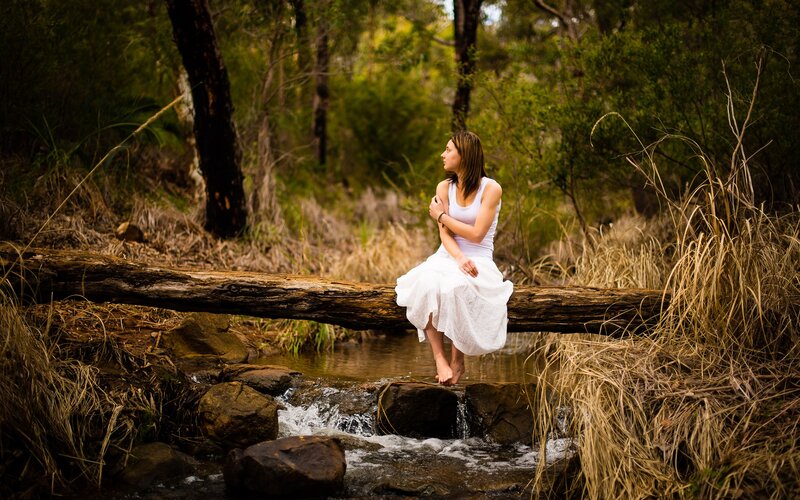 Woman sitting on log by stream