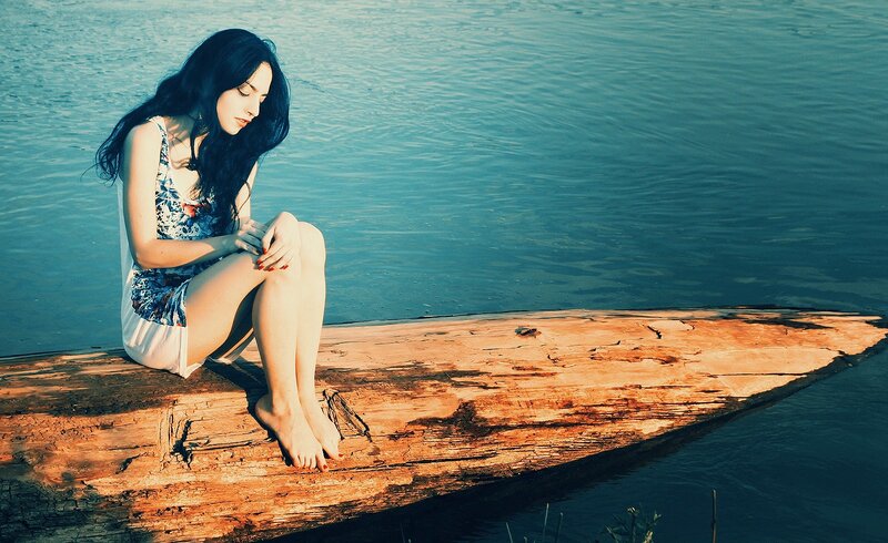 woman sitting on log by water