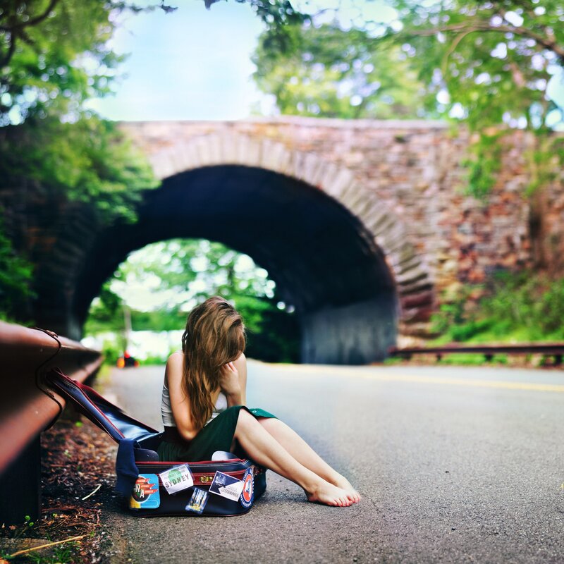 woman sitting on road with suitcase
