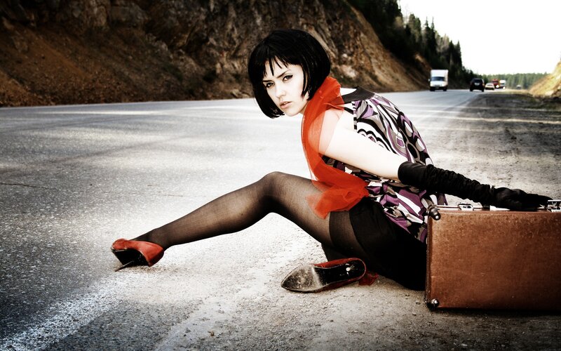 woman sitting on road with suitcase