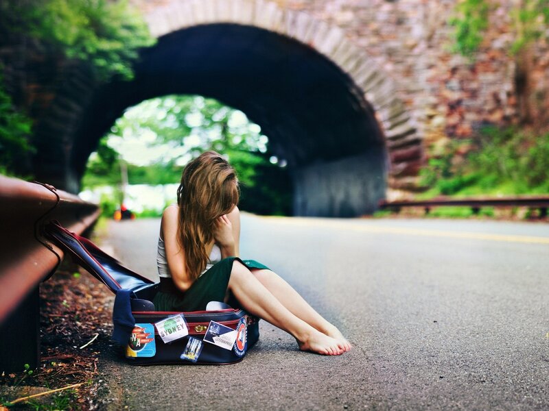 woman sitting on road with suitcase