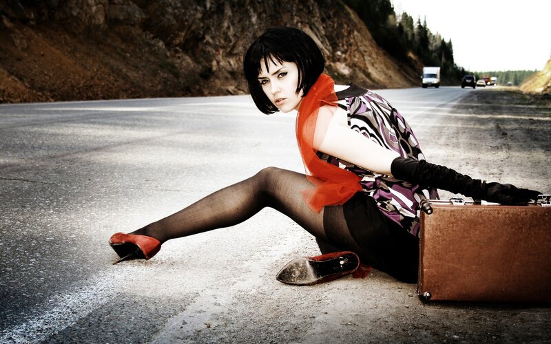 Woman sitting on road with suitcase