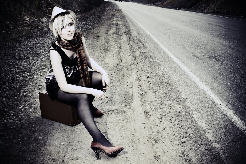 woman sitting on suitcase by road