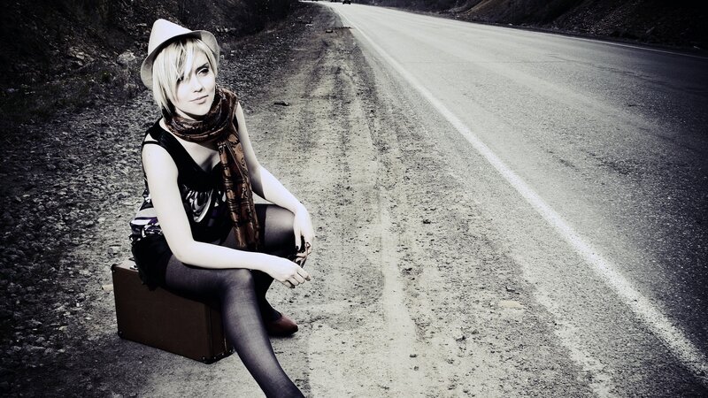 woman sitting on suitcase by road