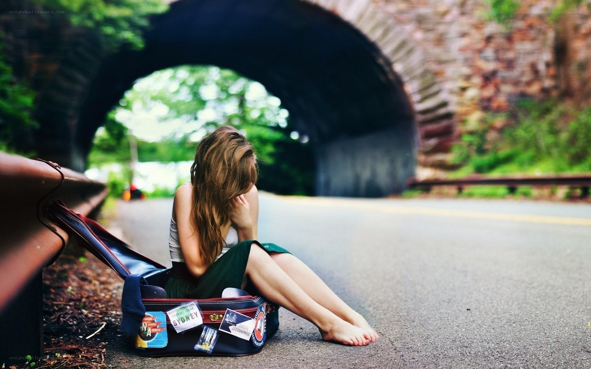 Woman sitting on suitcase by road