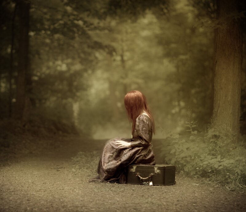Woman sitting on suitcase in forest