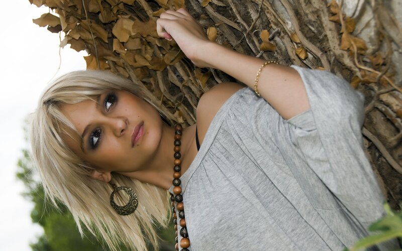woman with blonde hair leaning against tree