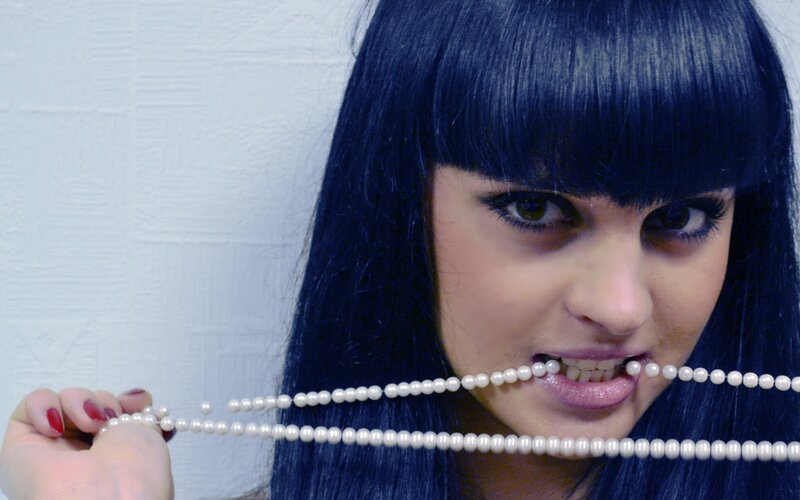 woman with blue hair biting pearls