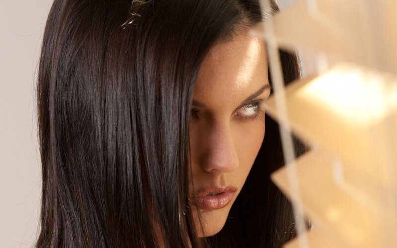 woman with dark hair looking through blinds